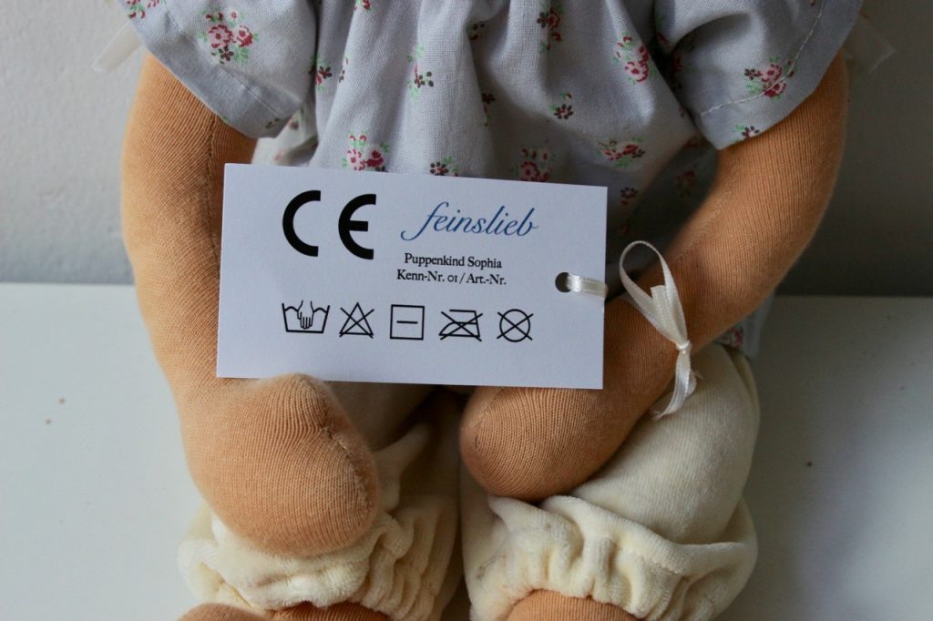 Detail einer Waldorfpuppe / Stoffpuppe / Puppe mit CE-Etikett (Vorderseite). Hier sid die Textilpflege-Symbole richtig dargestellt (Reihenfolge).