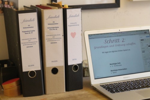 Drei Ordner mit CE-Unterlagen und ein Laptop, der "Schritt 2" des CE-Handbuches anzeigt.
