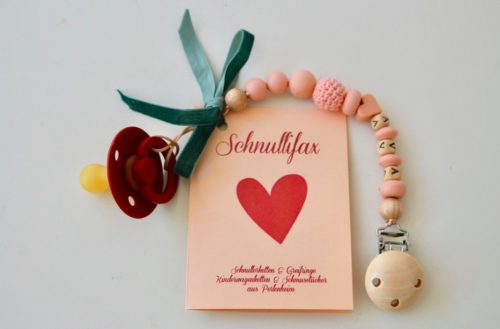 Vorderseite eines Beipackzettels für Schnullerketten mit Warnhinweisen, mit Text "Schnullifax" und einem roten Herz als Logo