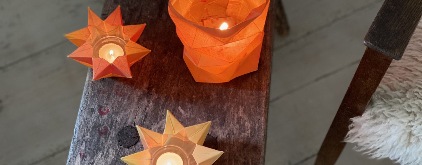 Drei gefaltete Sternenlichter bzw. Laternen auf Holzhocker