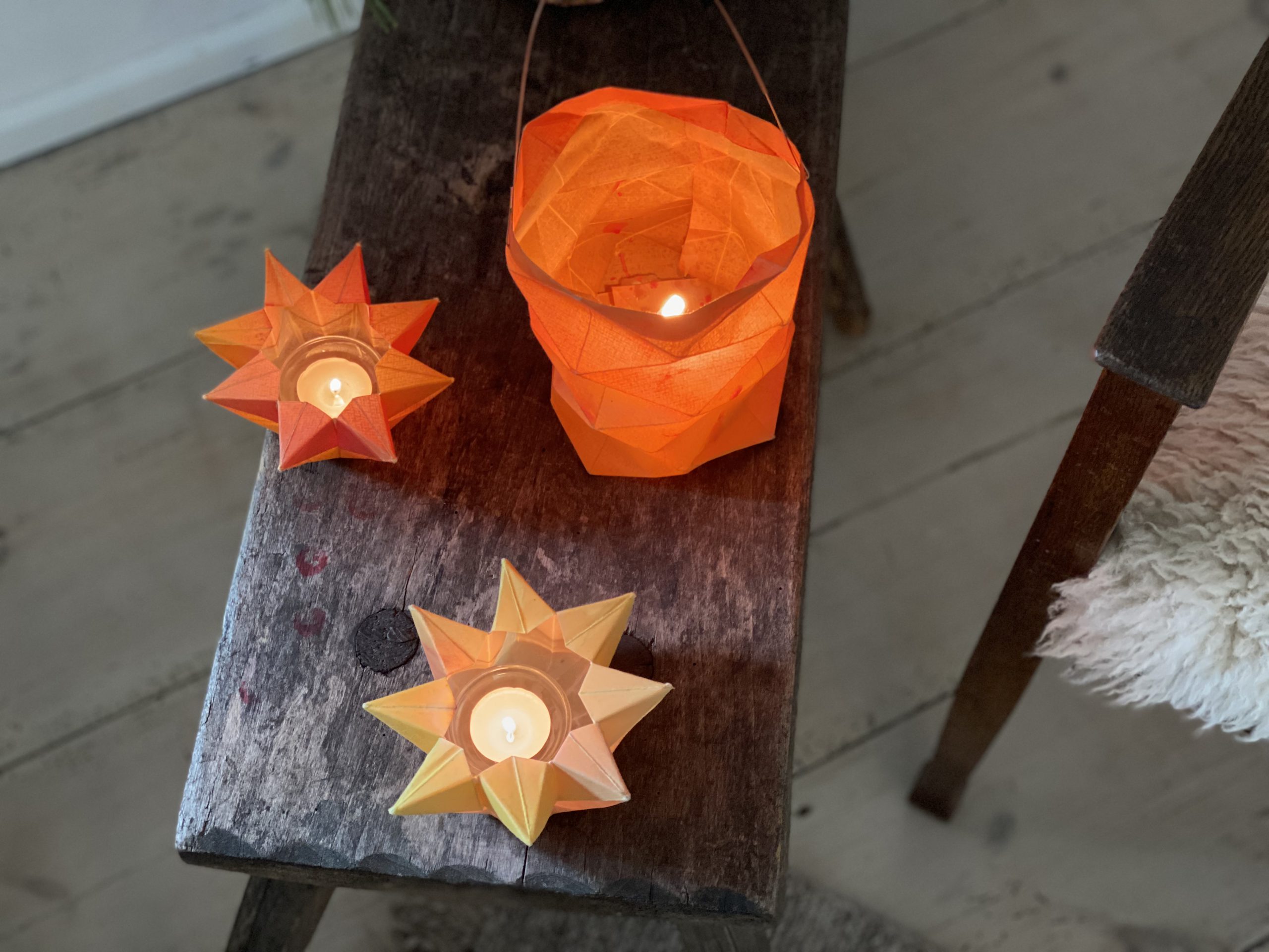 Drei gefaltete Sternenlichter bzw. Laternen auf Holzhocker