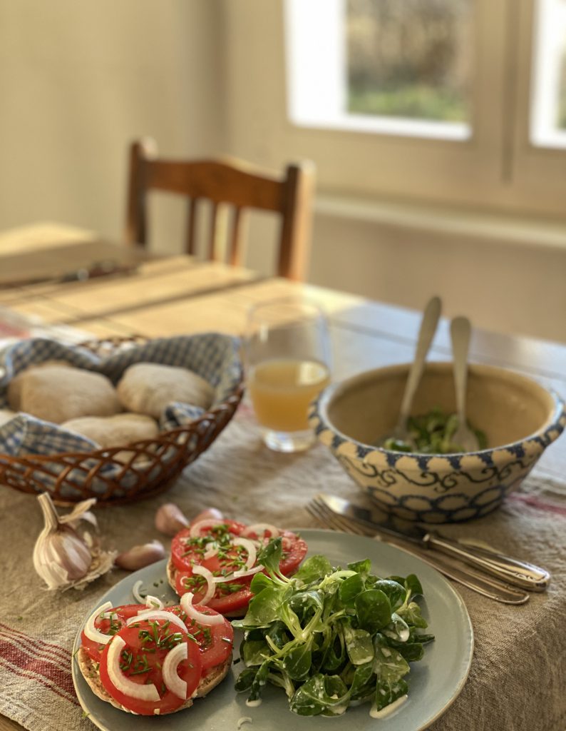 gedeckter Tisch mit Feldsalat, Tomatenbrötchen, Apfelsaft im Glas und Brötchenkorb