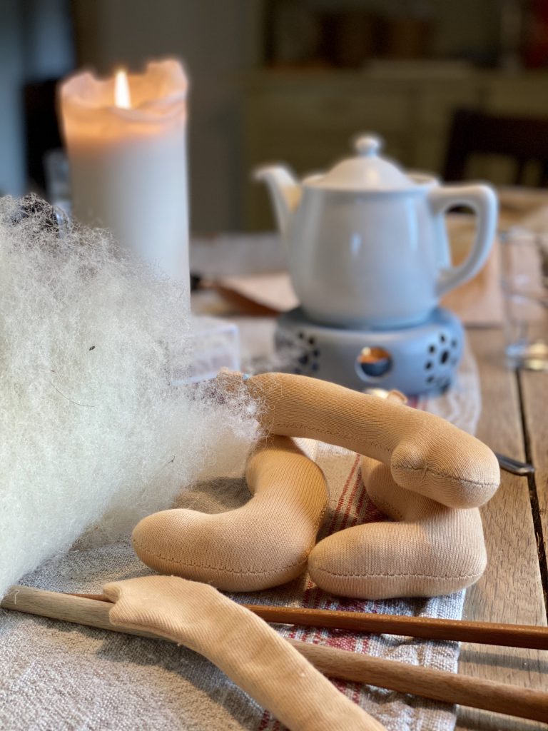 Puppen-Gliedmaßen vor Teekanne und Kerze auf Holztisch