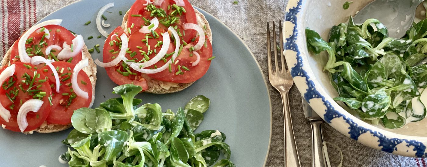 Gedeckter Tisch mit hellblauem teller, darauf Feldsalat und Tomatenbrötchen