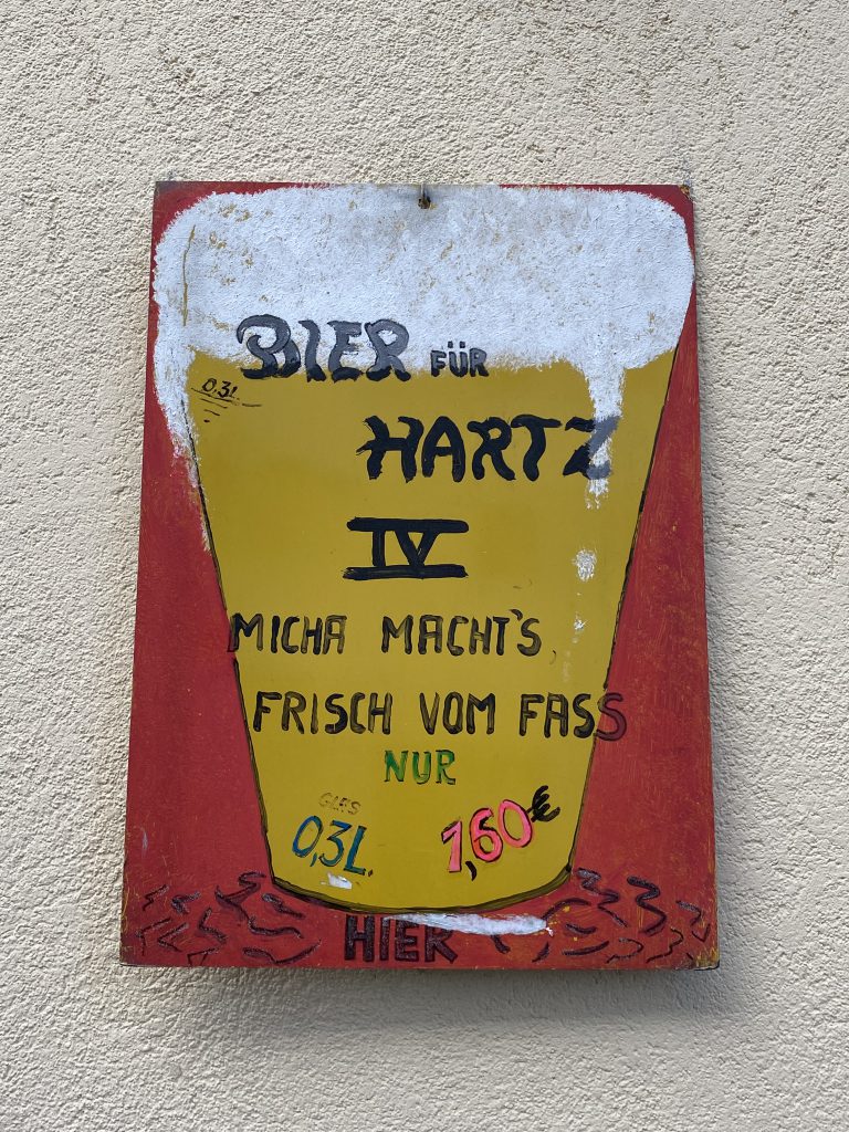 Ein perfekter Tag in Berlin ist für manche an Bier gekoppelt: Spruch-Tafel: "Bier für Hartz 4 - Micha macht's- Frisch vom Fass - 0,3 l nur 1,60