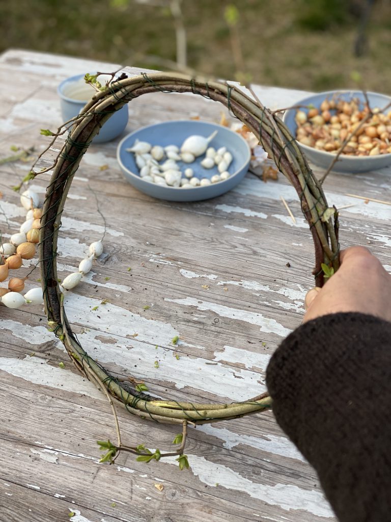 Dekoration mit Steckzwiebeln: Kranz aus Zweigen und mit Steckzwiebel-Ketten verziert, vertikal stehend auf Gartentisch