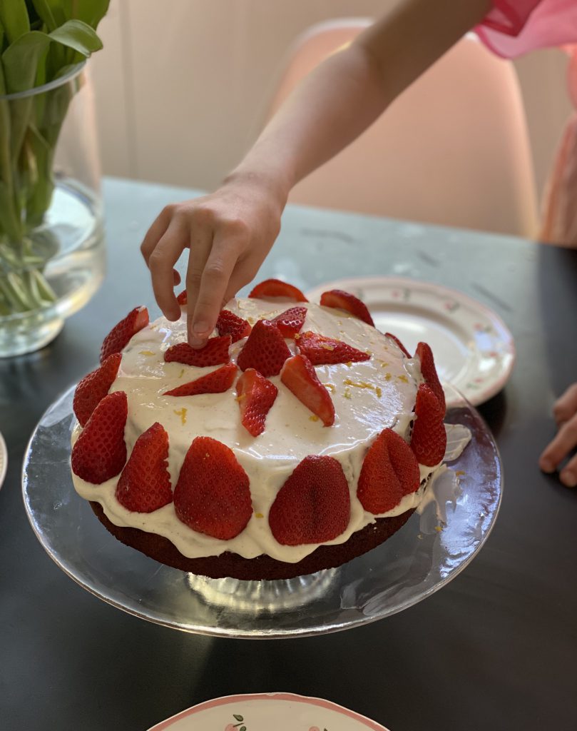 Kinderhand legt Erdbeere auf Torte: Backen und andere kreative Tätigkeiten sind auch ein Beispiel für das Gute an der Corona-Krise.