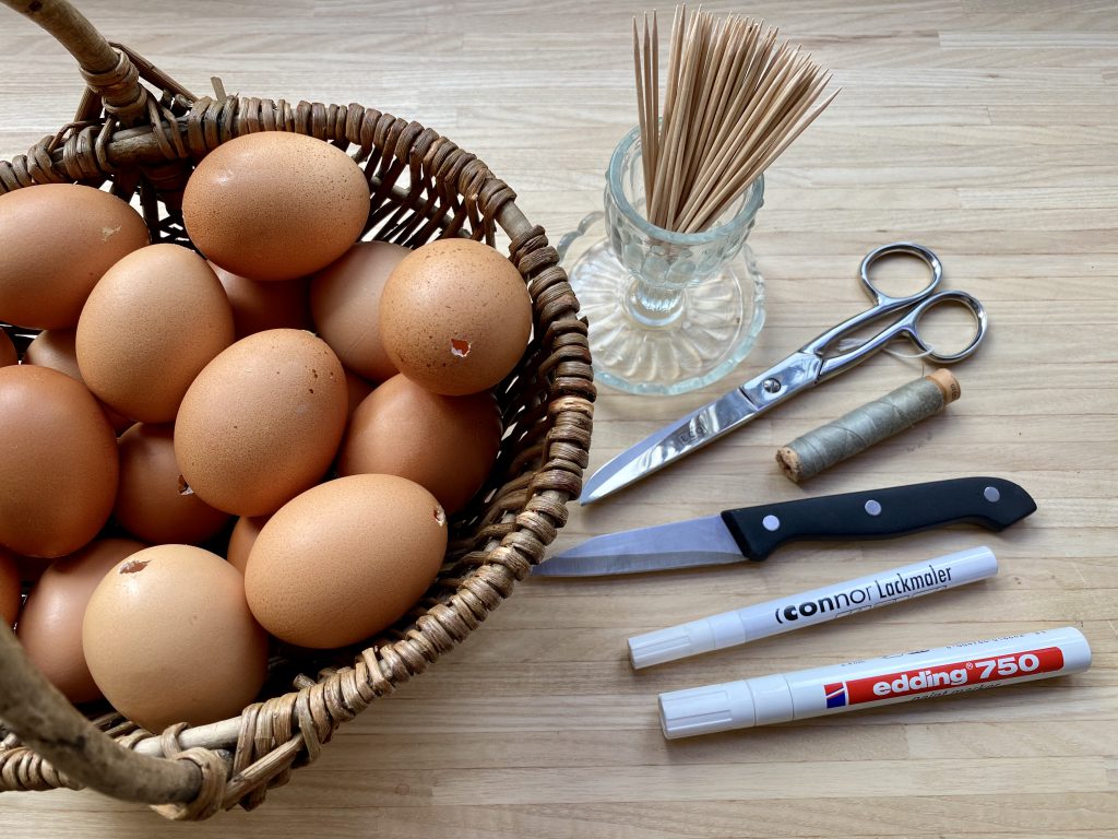 Korb mit ausgeblasenen Eiern und alles benötigten Materialien, um braune Eier am Osterstrauß herzustellen