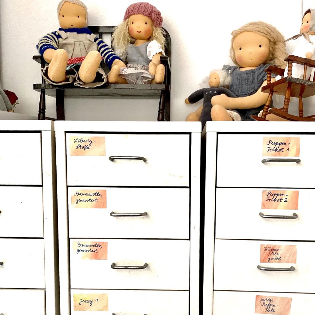 Schubladenschrank mit Puppen darauf. Jede Schublade trägt eine Beschriftung, was drin ist. Ordnung schaffen ist auch etwas Gutes an der Corona-Krise.