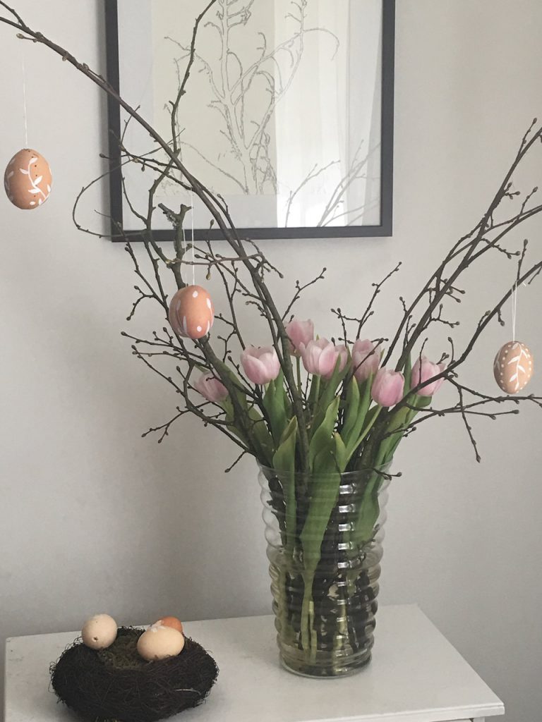 verschiedene weiß verzierte Eier an Obstbaumzweigen mit rosa Tulpen