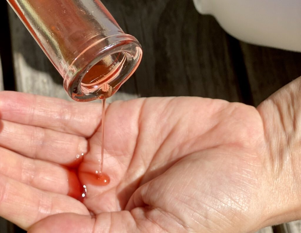 Johanniskrautöl selbst herstellen: Rotes Öl tropft aus einer Flasche in die Handfläche