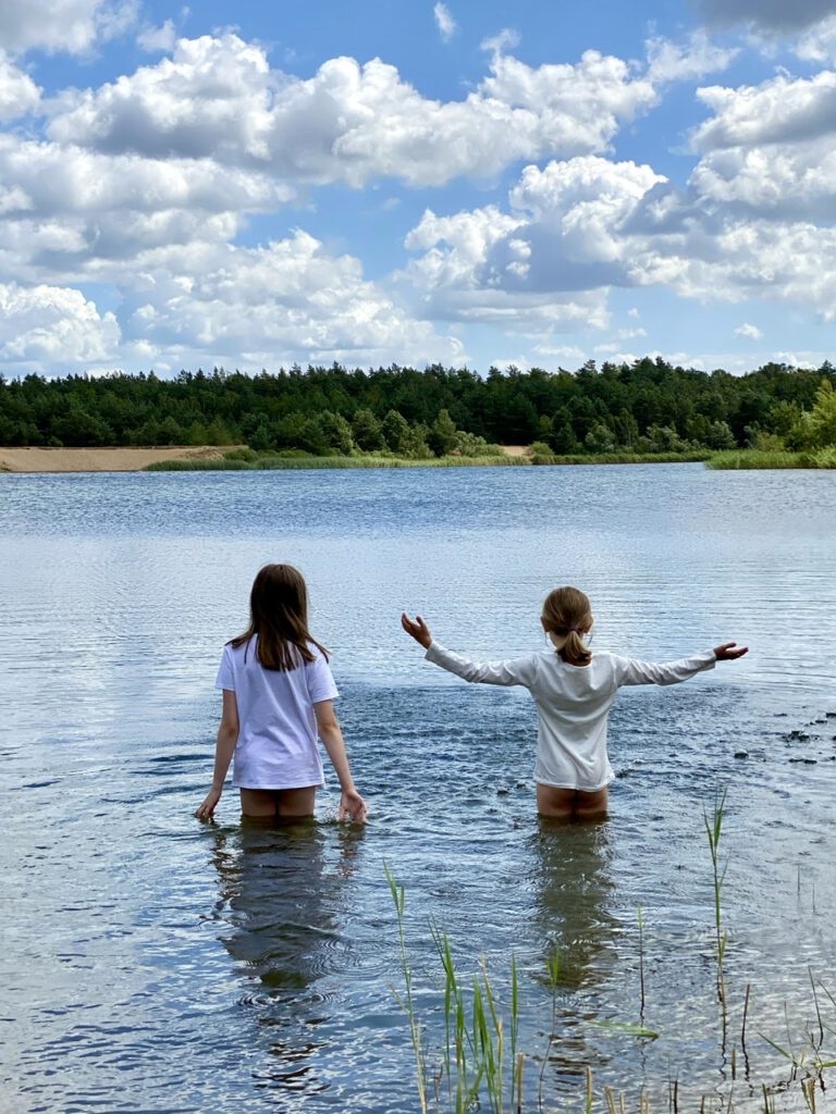 Meine beiden Kinder bis zum Popo im See stehend, mit T-Shirts an.