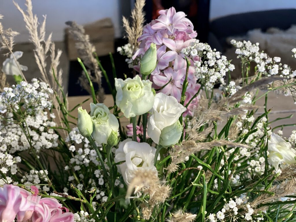 Winterstrauß mit Lysianthus, rosa Hyazinthen, Schleierkraut. Kiefernzweigen und Gräsern auf hellem Holztisch