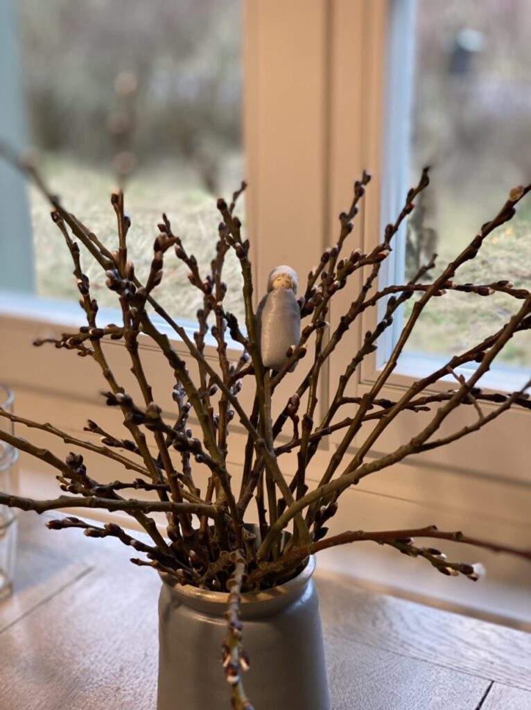 Ein Weidenkätzchen-Blumenkind in einem kleinen Weidenstrauß auf einem Holztisch, von vorne