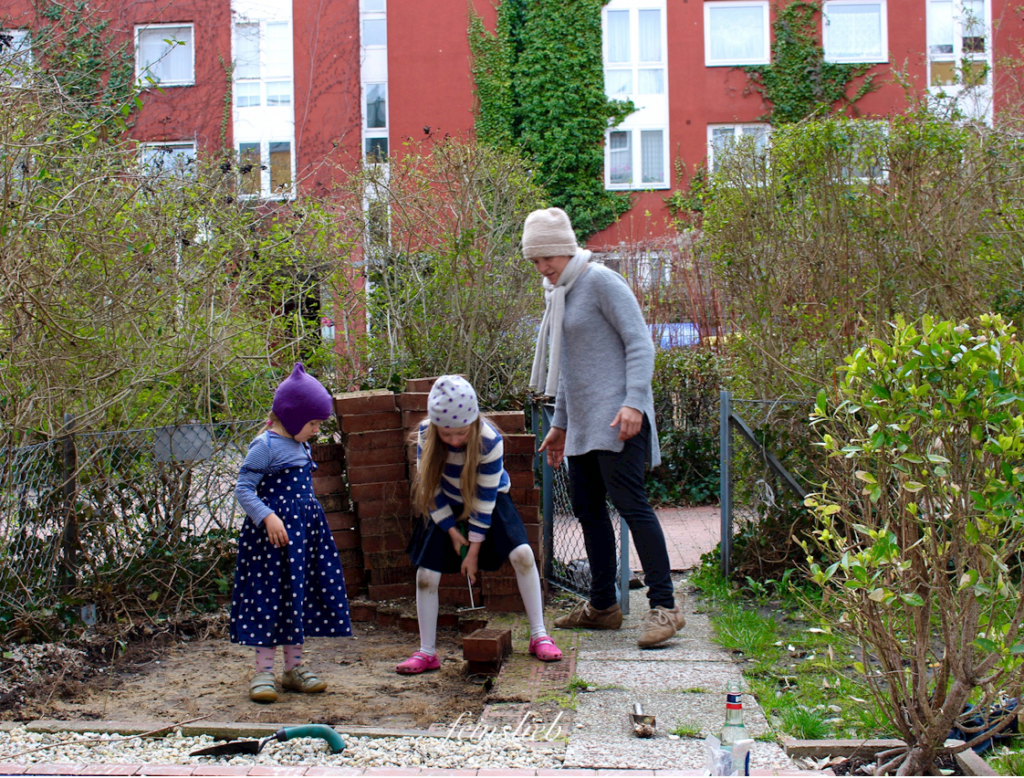 Umgestaltung des Gartens der Wohnung in Berlin: 2 Kinder hebeln Steinplatten aus dem Sandboden.