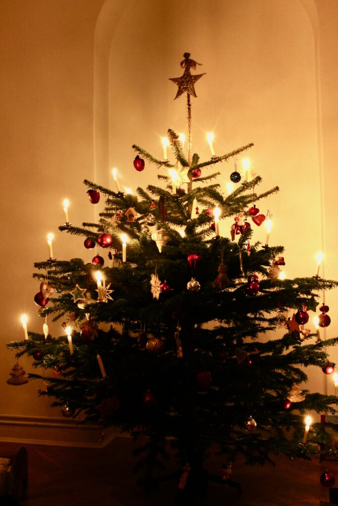 Weihnachtsbaum mit vielen echten Kerzen, roten Kugeln und Strohsternen: Weihnachten ohne Stress, dabei helfen auch echte Kerzen