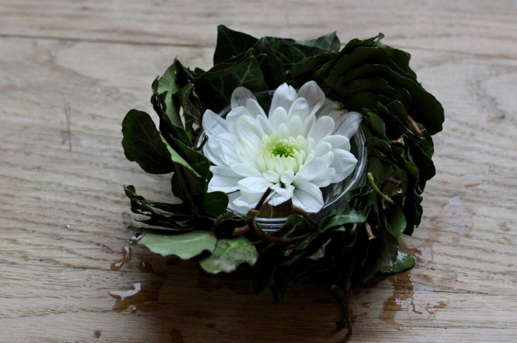 Dekorieren mit Efeu: kleiner weiße Blüte in Glasschüssel, umrahmt von Efeu-Kranz