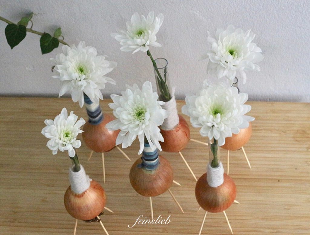 Winterliche Dekoration: Chrysanthemen-Blüten in kleinen Vasen auf normalen Küchenzwiebeln.