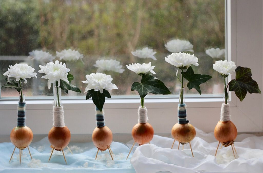Dekorieren mit Efeu: 6 Zwiebel-Vasen mit weißer Blüte und Efeu auf Fensterbrett.