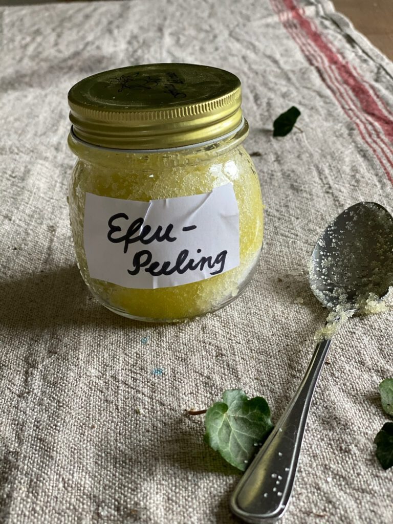 Glas mit hellgrünem Efeu-Peeling und Zuckerlöffel, auf Leinen