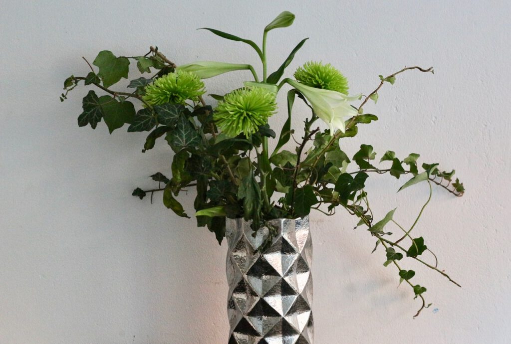 Dekorieren mit Efeu: Strauß aus weißer Lilie, hellgrünen Chrysanthemen und Efeu-zweigen in silberner Vase.