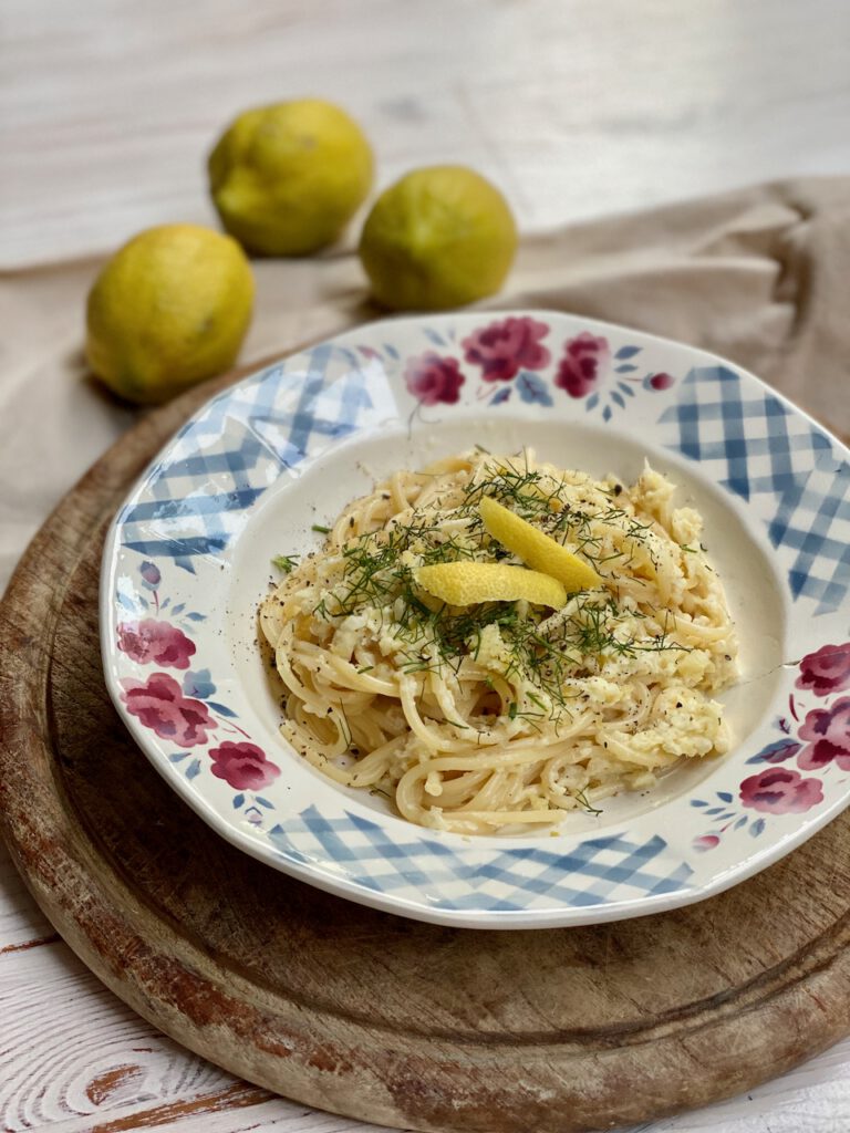 Beste Rezepte mit Zitronen: Tiefer Teller mit Zitronen-Fenchel-Pasta auf rundem Holzbrett, dahinter 3 Zitronen