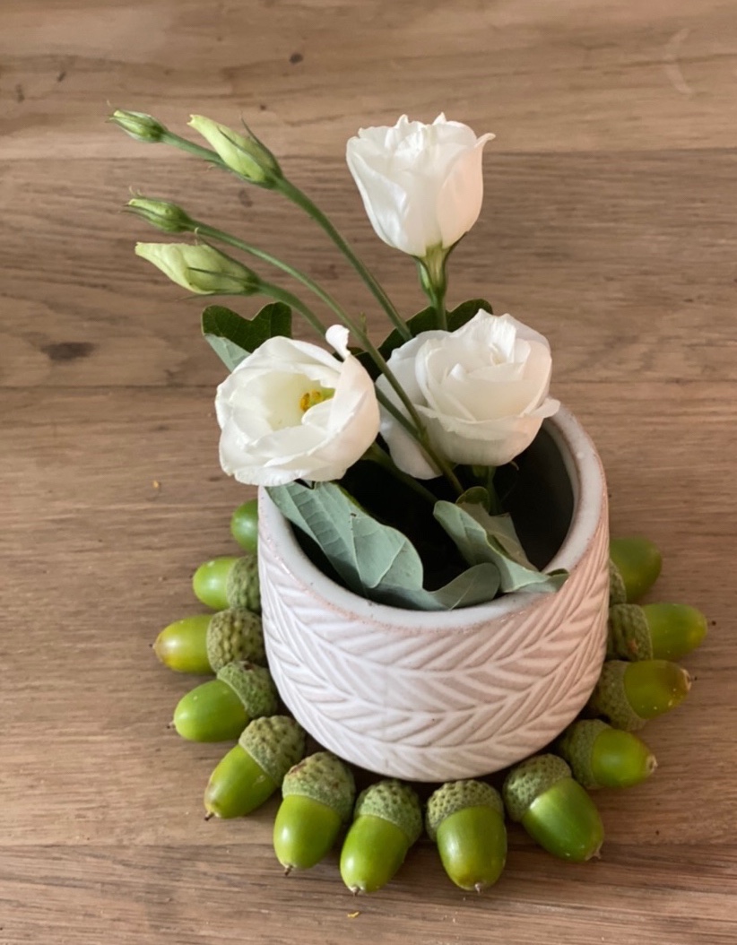 Basteln mit grünen Eicheln Idee 3: Ein Kranz aus nebeneinander liegenden grünen Eicheln um ein Väschen mit Lysianthus-Blüten