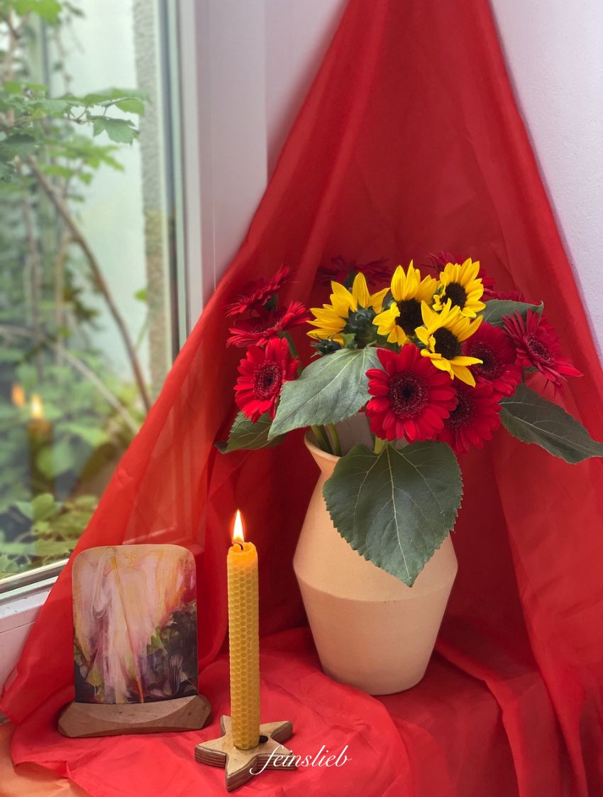 Jahreszeitentisch Michaeli schlicht: Rotes Tuch in Ecke, Vase mit Sonnenblumen, Bienenwachskerze, Postkarte mit Michael in Holzständer