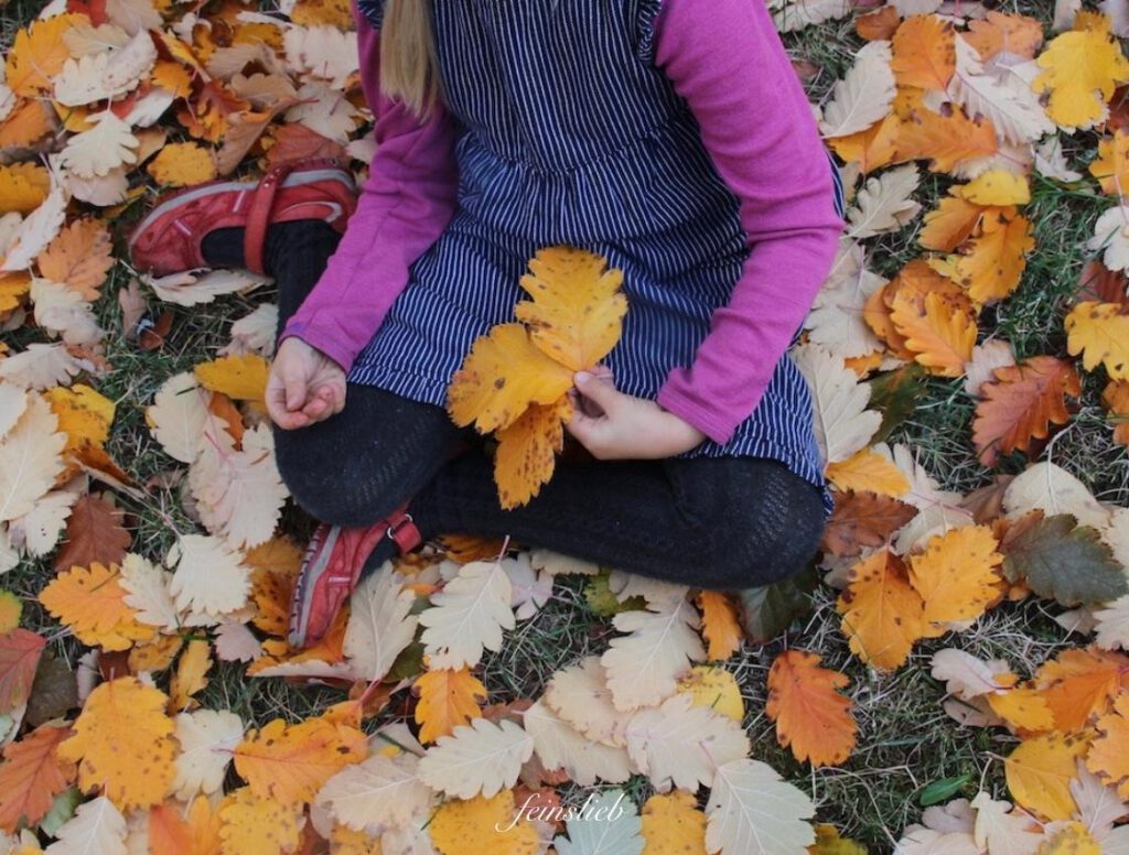Kind sitzt in bunten Blättern und hat 3 bunte Blätter im schoß
Oktober mit Kindern