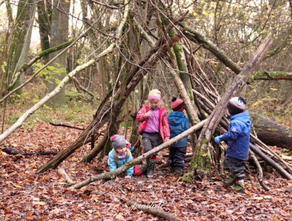 Kinder in einer selbst gebauten Holzhüte im Wald (September Ideen für Aktivitäten mit Kindern)