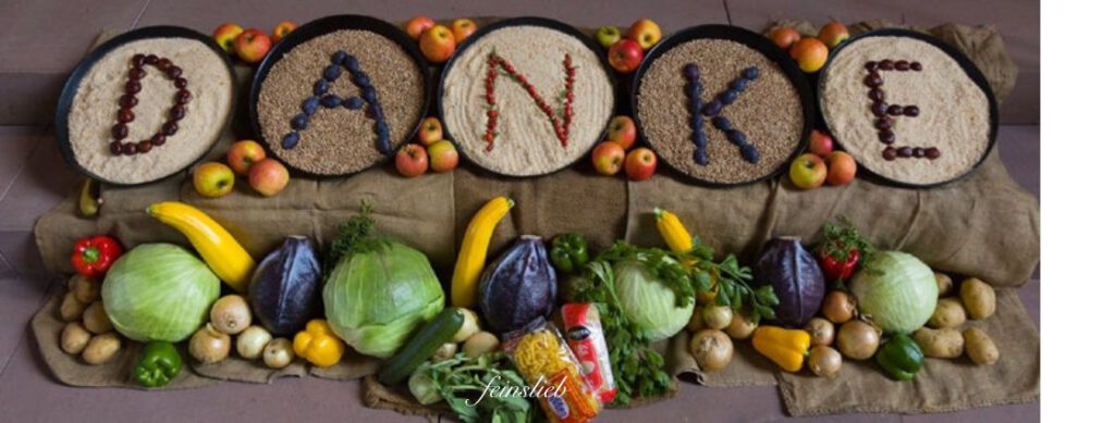 Erntedank-Installation mit Früchten und Gemüse und tellern, in denen aus Beeren jeweils ein Buchstabe gebildet ist, die zusammen das Wort DANKE ergeben.