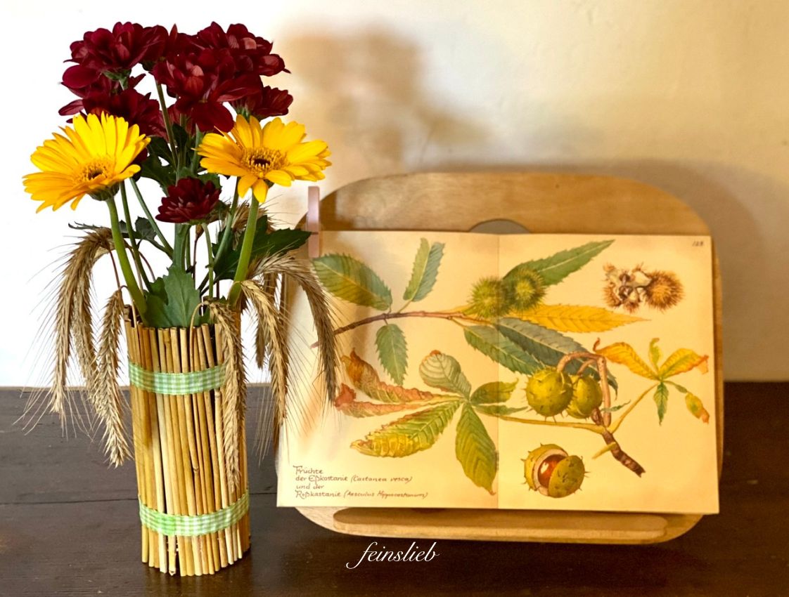 Jahreszeitentisch September mit Vase aus Getreideähren und aufgeschlagenem Buch/Bild mit Kastanien 