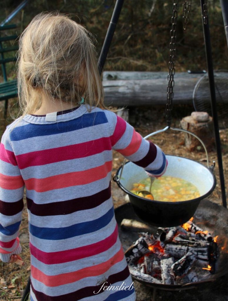 Kind kocht Suppe über einem Feuer im Garten.