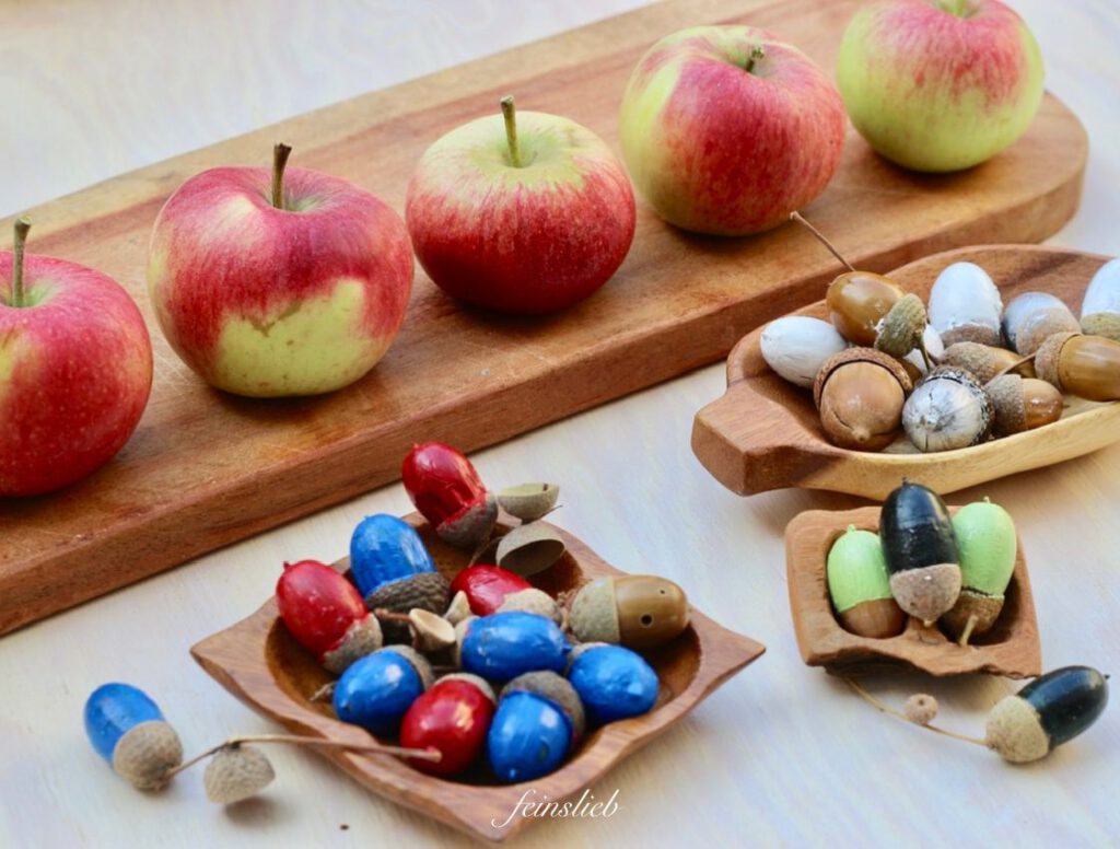 Angemalte Eicheln vor Äpfeln auf weißem Tisch
(September Bastel-Idee für Kinder)