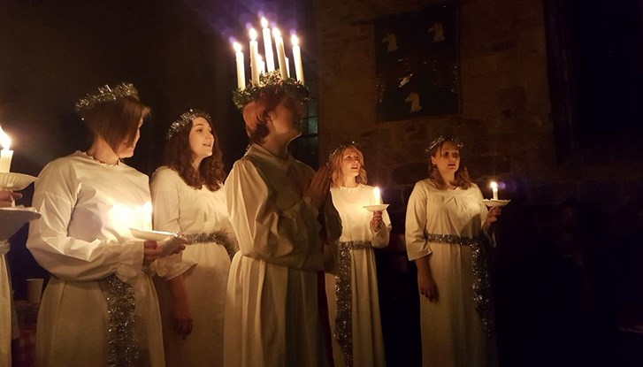 Lucia feiern: Gruppe von Mädchen in dunkler Umgebung in weißen Kleidern, eine trägt Lichterkranz.