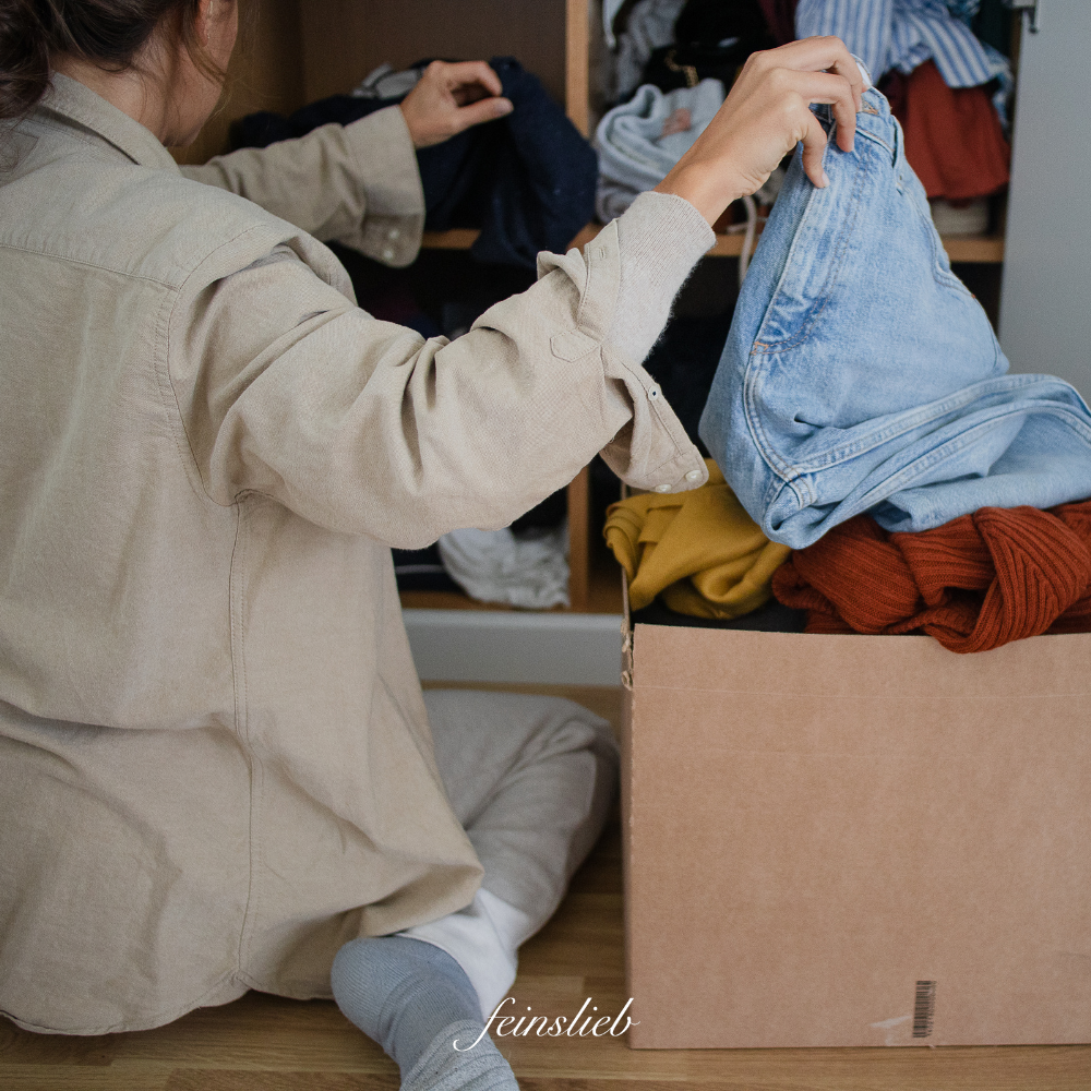 Ausmisten als Aktivität im März: Frau vor einem Schrank legt Kleidungsstücke in Karton