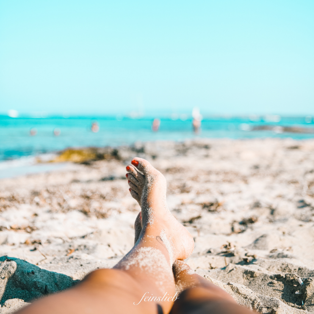 übereinandergelegte Füße mit Sand dran am Strand vor Meer in der Sonne