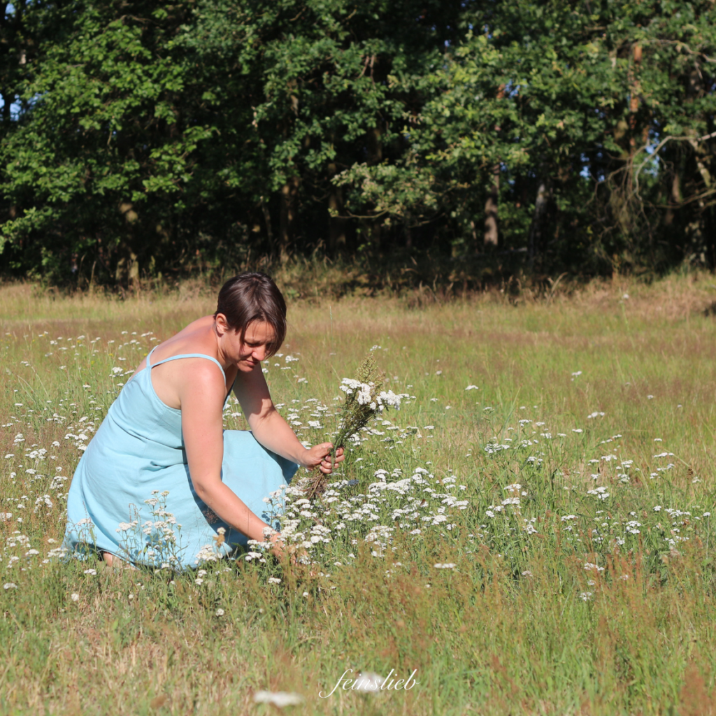 Maike pflückt auf einer Juli-Wiese vor Waldrand weiße Blumen